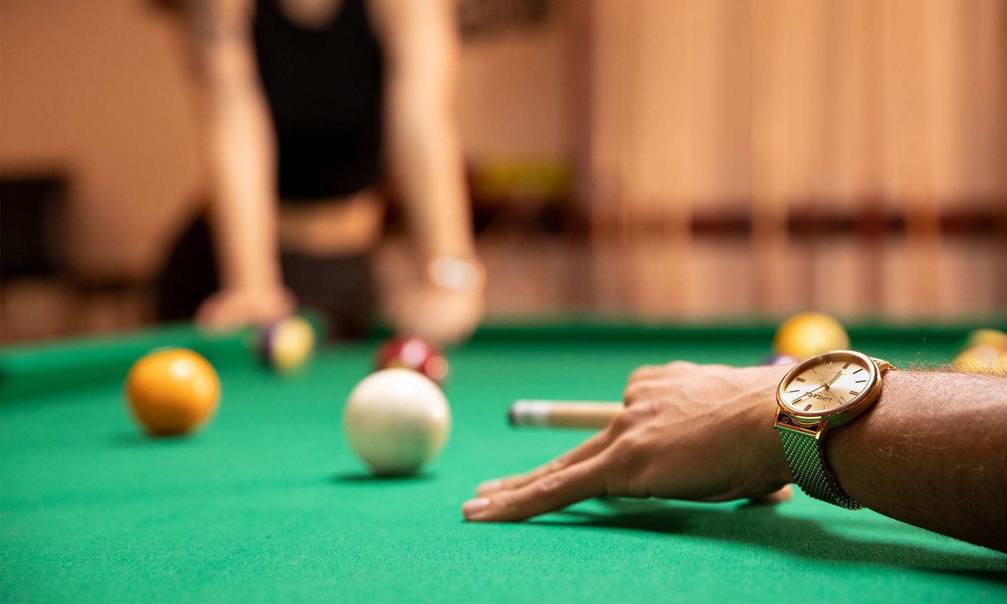 arm wearing gold watch lining up a shot on pool table with green felt